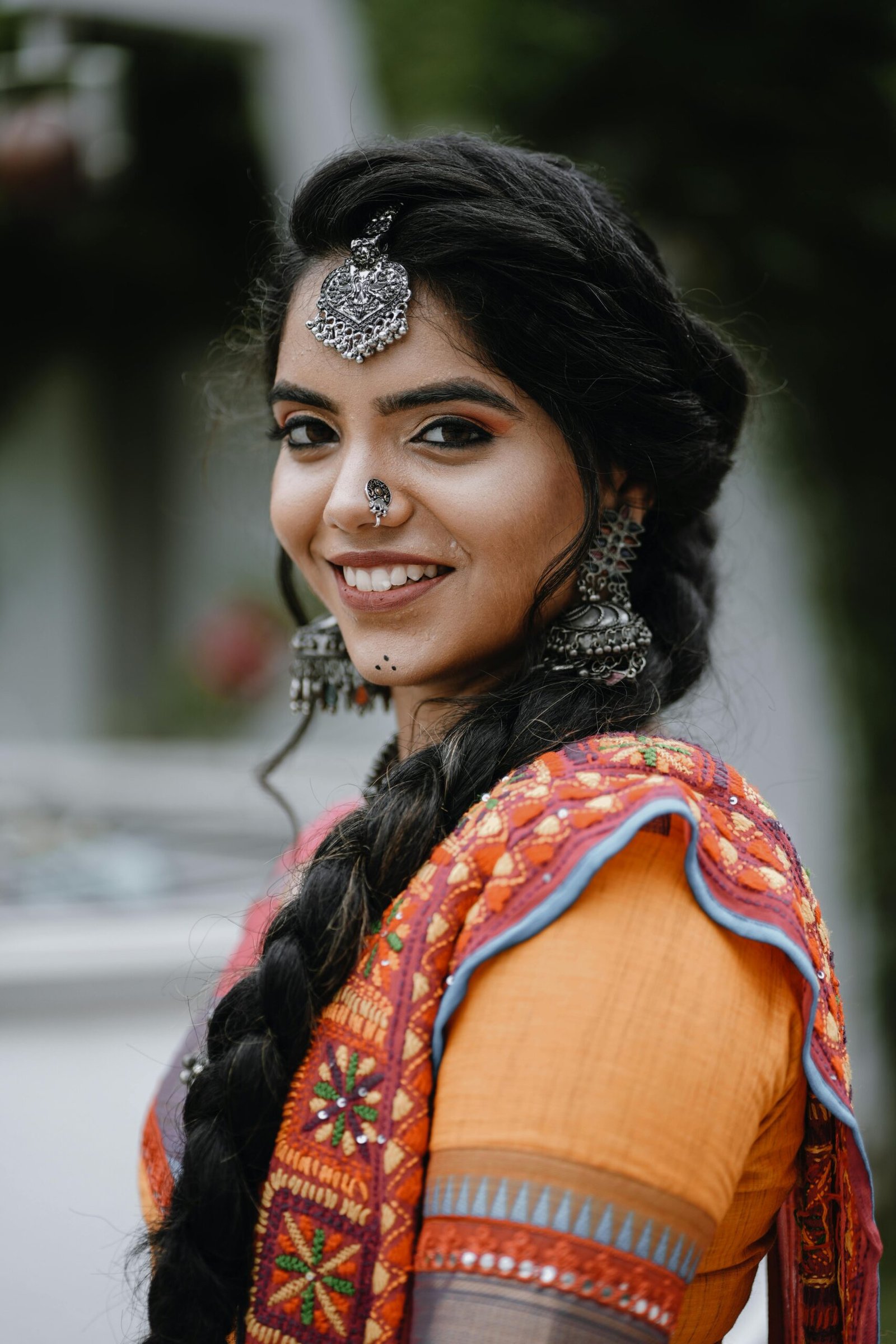 Portrait of a young woman in vibrant traditional Indian attire, smiling outdoors.